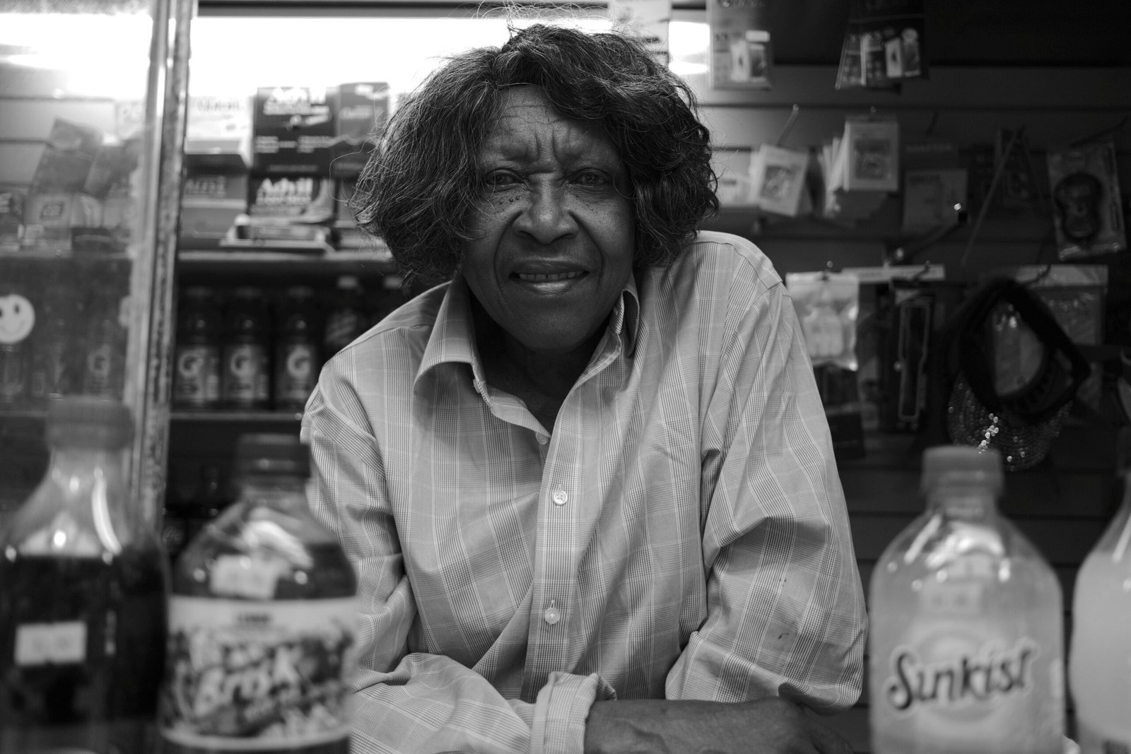 cover - photography Black and white portrait of a smiling woman behind a corner store counter