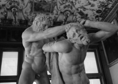 Black and white photo of two wrestling marble statues beneath a frescoed ceiling