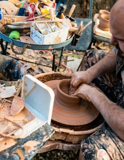 Potter shaping a wet clay vessel on the wheel, surrounded by tools