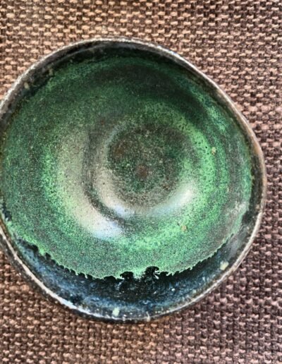 Hand-thrown bowl with mottled moss-green glaze and a dark speckled rim